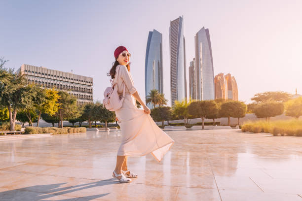 A woman in fashionable attire enjoys the urban landscape of Dubai, with towering skyscrapers in the background.