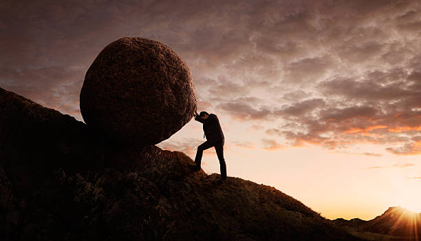 Entrepreneur pushing a large boulder uphill symbolizes common challenges faced when starting a small business.