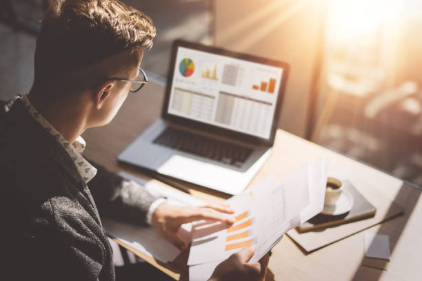 A person reviews financial reports and charts on a laptop and papers, highlighting efficient business management tips.